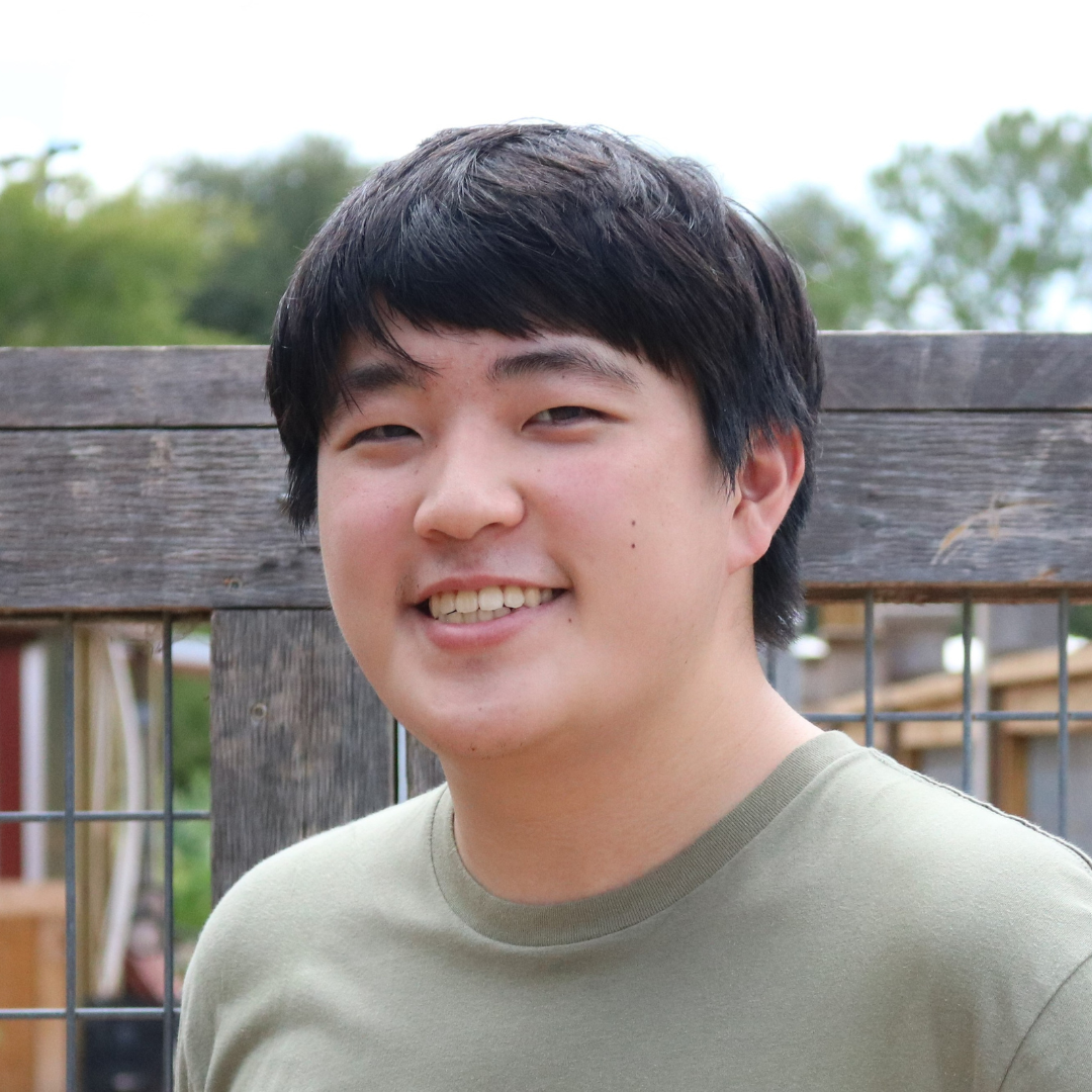 A man with straight, black hair is smiling at the camera while wearing a green t-shirt