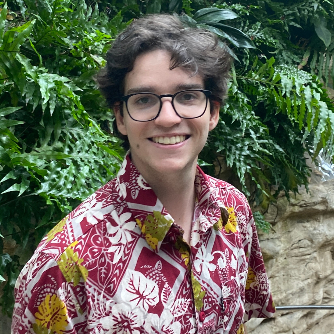 A man with short, curly brown hair is wearing black glasses and a red Hawaiian shirt