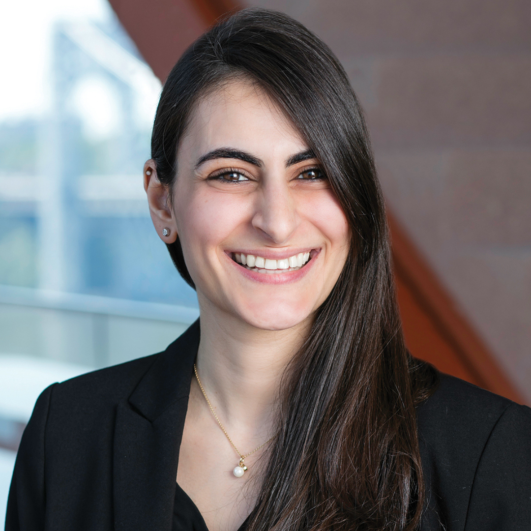 A woman with long, dark brown hair is seen smiling at the camera