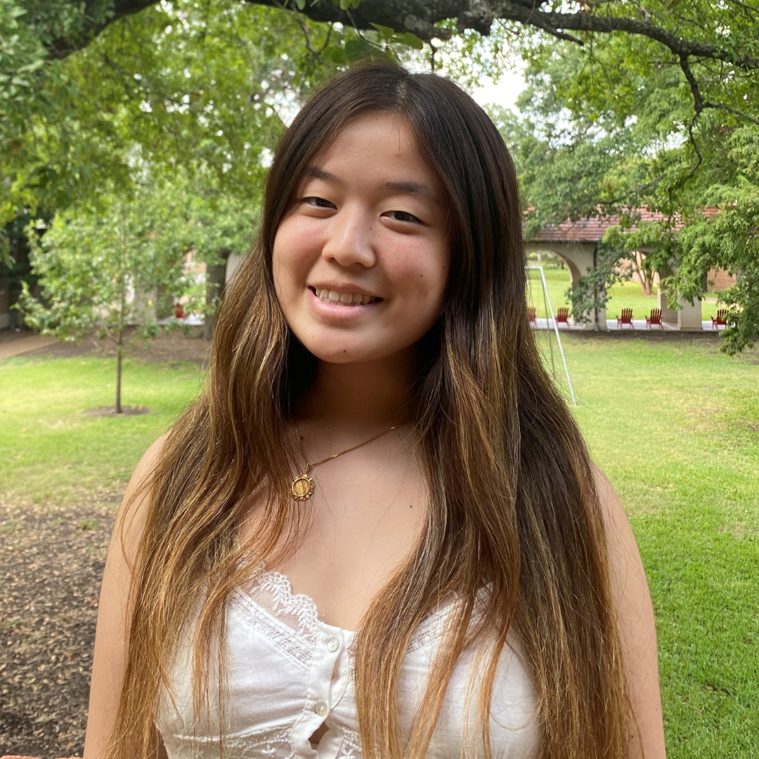 A woman with black, long straight hair and wearing a white tank-top is shown smiling at the camera.