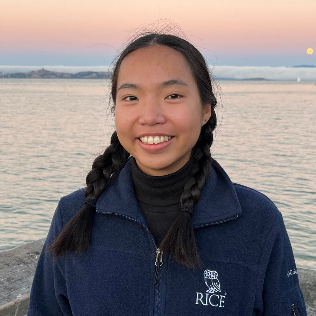 A woman with black french braided hair is wearing a Rice University jacket and smiling at the camera
