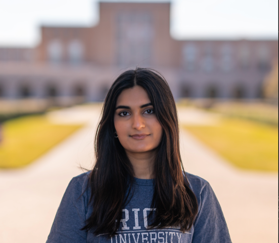 A girl with long, straight brown hair is staring into the camera and wearing a Rice University sweater