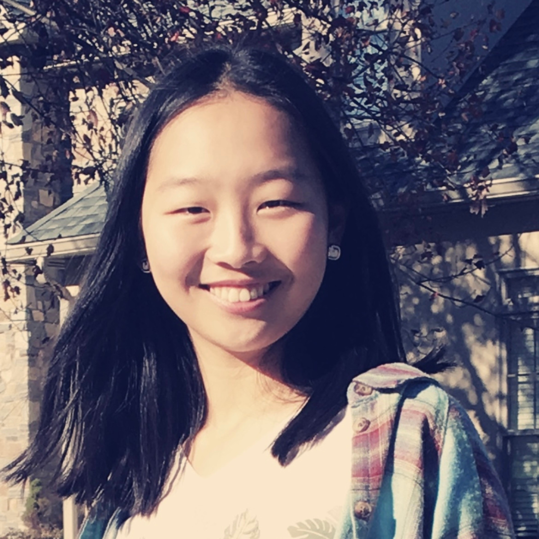 A woman with long, straight-black hair is smiling at the camera and wearing a flannel shirt over a white t-shirt