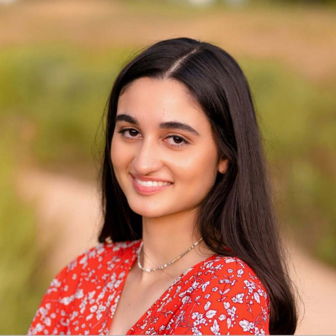 A female student with long, brown hair is smiling at the camera. She is wearing a red blouse with white flowers on it