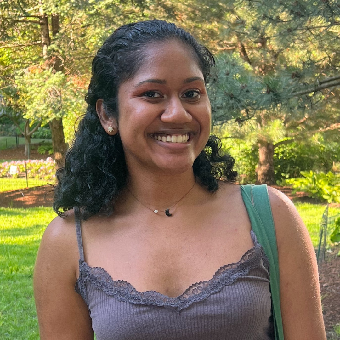 A female student with short, curly black hair is smiling at the camera and wearing a brownish-gray camisole top