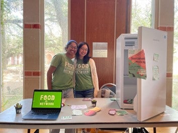 Two female students hug for a photo behind a table highlight the Food Recovery Network's mission