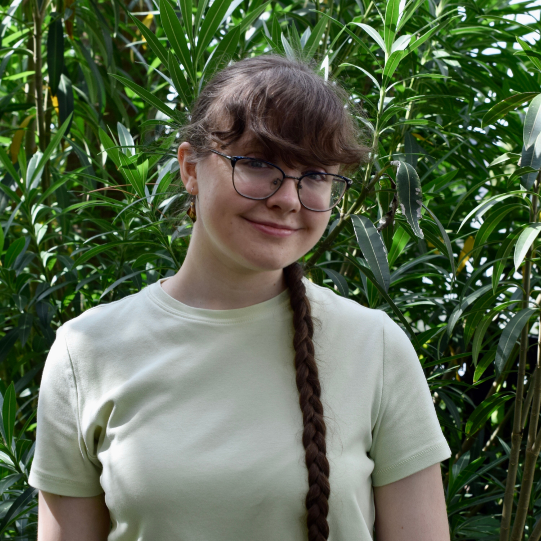 A female student is wearing glasses and a beige t-shirt. She has really long, dark brown hair that is braided across her shoulder