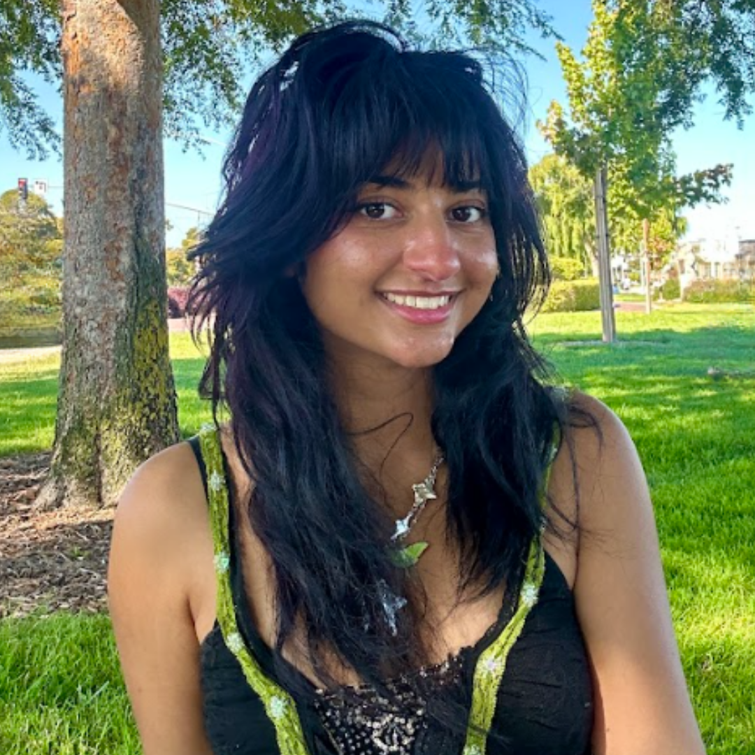 A female student with long, wavy black hair and bangs is smiling at the camera and wearing a black and gold tank top