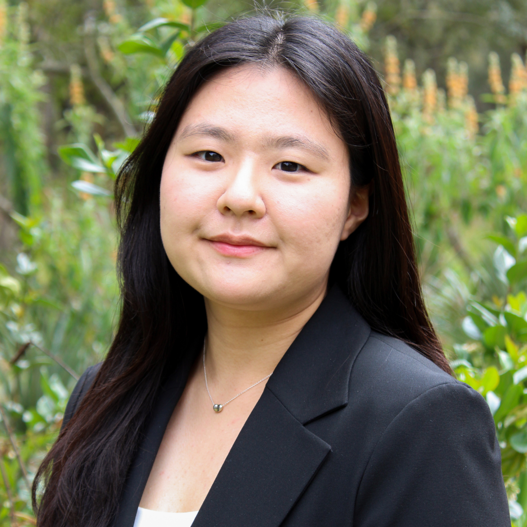 A female student with long, straight black hair is smiling slightly at the camera. She is wearing a white blouse and black blazer