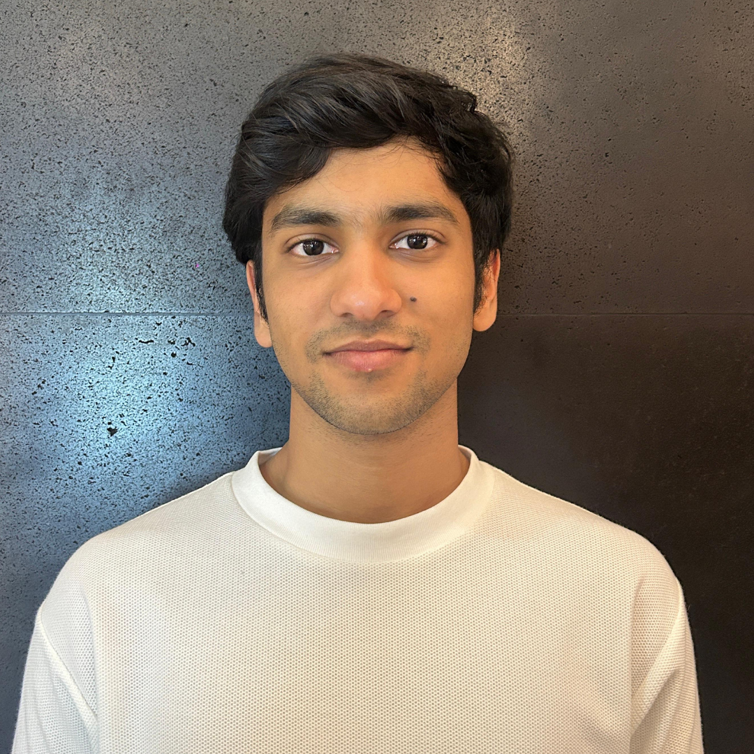 A male student with dark brown eyes and black hair is looking into the camera with a slight smile. He is wearing a white shirt against a dark background.