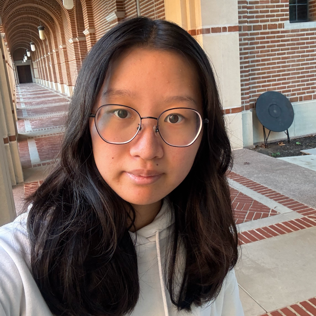A female student with glasses and long, straight black hair is smiling slightly while looking at the camera. She is wearing a light gray hoodie.